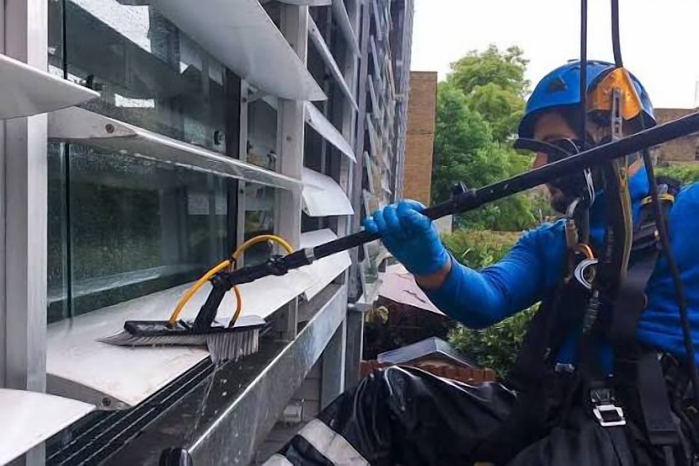 Window cleaner on ropes using a long-handled brush